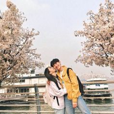 two people standing next to each other in front of some trees with flowers on them