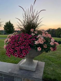 a large vase filled with lots of flowers on top of a cement block in the grass