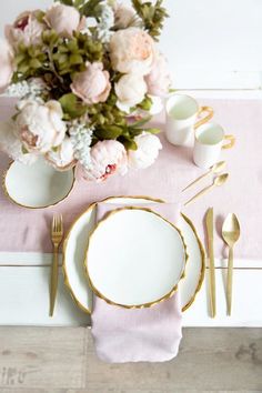 the table is set with white and gold plates, silverware, and pink napkins