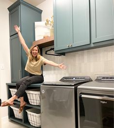 a woman sitting on top of a washer next to a dryer in a laundry room