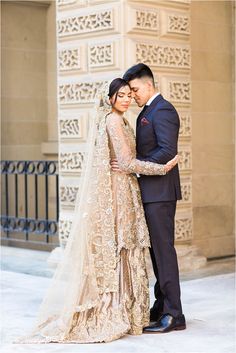 a bride and groom pose for a photo in front of an ornate wall with intricate carvings