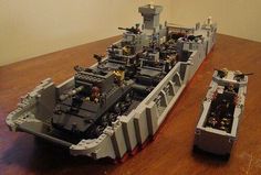 two legos are sitting on a table next to a large ship that is made out of lego blocks