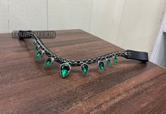 a black choker with green stones on it sitting on a wooden table next to a window