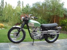 a green motorcycle parked on top of a stone walkway in front of some grass and trees