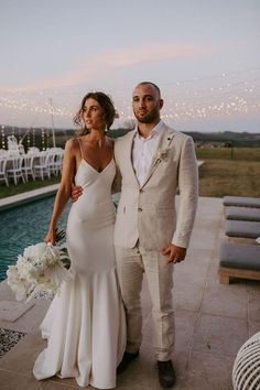 a bride and groom standing next to each other in front of a pool at sunset