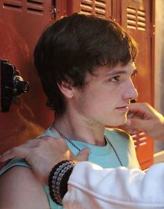 a young man adjusts his watch while standing in front of a locker with red doors