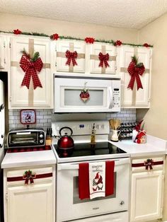 a kitchen decorated for christmas with white cabinets and red bows