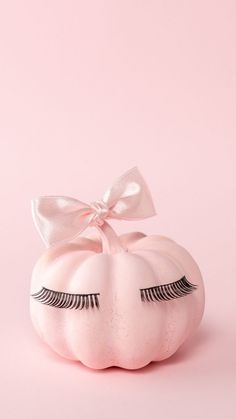 a white pumpkin with eyelashes and a bow on it's head, against a pink background