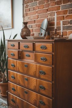 a wooden dresser with many drawers in front of a brick wall and potted plants