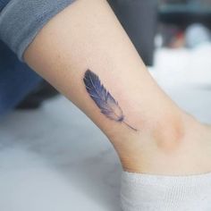 a person with a tattoo on their foot that has a small blue feather on it