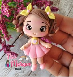 a hand holding a small doll with flowers in the background