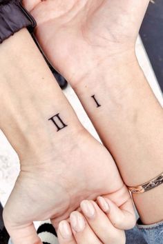 two people are holding hands with tattoos on their wrists and one has the letter i in roman numerals