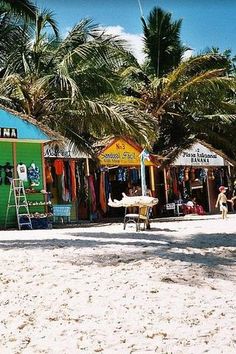 the beach is lined with brightly colored huts and palm trees, while people walk by