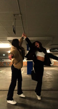 two women are hanging upside down in an empty parking garage, one is holding on to the pole