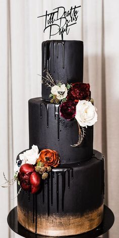 a black and gold wedding cake with flowers on top, dripping in the dark icing