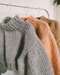 three sweaters hanging on a rack in front of a white wall