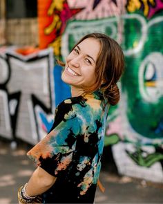 a woman standing in front of graffiti covered walls and smiling at the camera with her hand on her hip