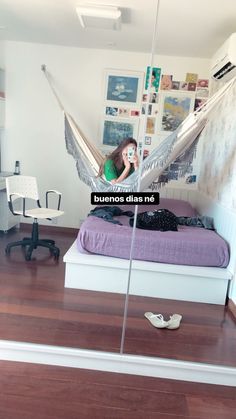 a woman sitting in a hammock on top of a bed next to a desk