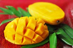 two pieces of mango sitting on top of green leaves next to each other and one piece cut in half