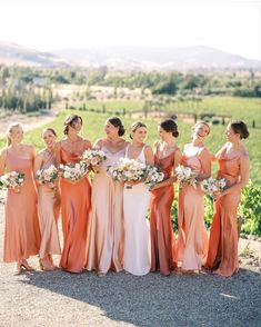 a group of women standing next to each other in long dresses and holding bouquets