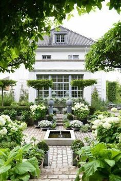 an outdoor garden with white flowers and greenery in front of a large house, surrounded by trees