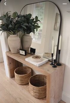 a wooden table topped with two baskets next to a large mirror and candle holders on top of it