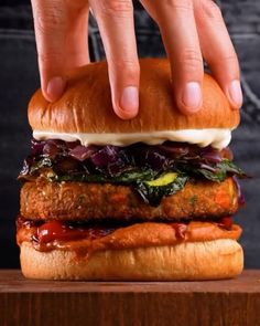 a hand reaching for a burger with meat and vegetables