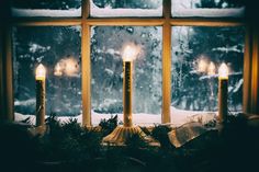 three lit candles sitting on top of a window sill in front of snow covered windows