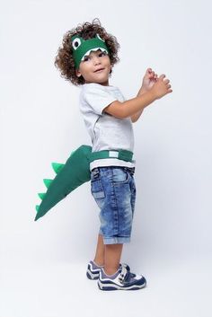 a little boy dressed up as a crocodile with a green mask and blue jeans, standing in front of a white background