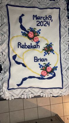 a cross stitch pillow with the names of two people and flowers on it hanging from a hook