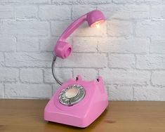 a pink telephone sitting on top of a wooden table next to a white brick wall