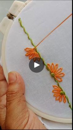 someone is stitching an orange flower on a white piece of fabric with green thread