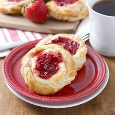 two small pastries on a red plate next to a cup of coffee and strawberries