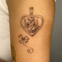 a cat in a heart shaped locke tattoo on the thigh with a clover and a bow