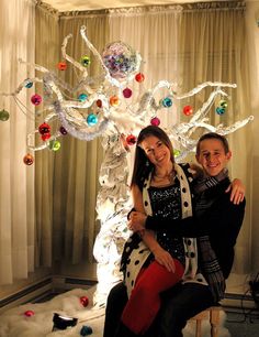 a man and woman sitting next to each other in front of a christmas tree with ornaments on it