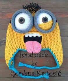 a crocheted hat with eyes and tongue sticking out from the front, on top of a wooden surface