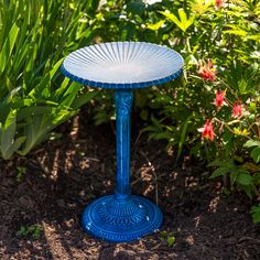 a blue bird bath sitting in the middle of some plants and flowers on the ground