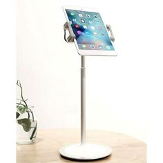 an ipad is sitting on top of a white stand in front of a potted plant