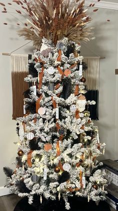 a white christmas tree decorated with orange and black ornaments, dried pamolite branches