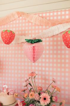 pink and white dessert table with strawberries hanging from the ceiling, flowers in vases next to cake