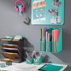 a white desk topped with lots of books and office supplies next to a gray wall