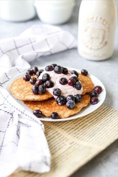 pancakes with blueberries and whipped cream are on a plate next to a bottle of milk