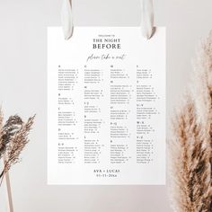 a white wedding seating plan hanging on a wall next to some dried plants and flowers