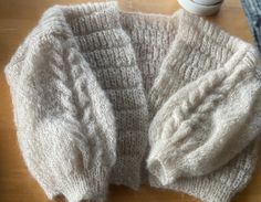 two knitted sweaters sitting on top of a wooden table next to a cup