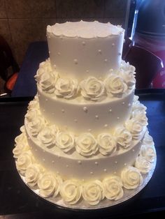 a three tiered cake with white roses on the bottom and sides, sitting on a table