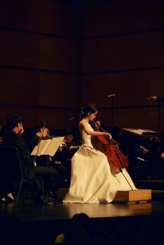 a woman in a white dress is playing the violin while others are sitting down behind her