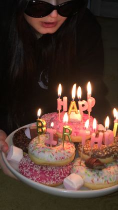 a woman holding a plate with donuts and lit candles on it that say happy birthday