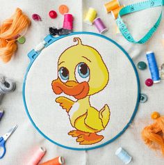 a cross stitch ducky is sitting on the table next to some thread and scissors