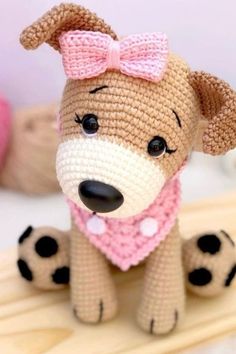 a crocheted dog with a pink bow sits on a wooden table next to stuffed animals