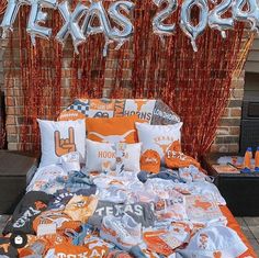 an orange and white bed with texas letters on it in front of a brick wall